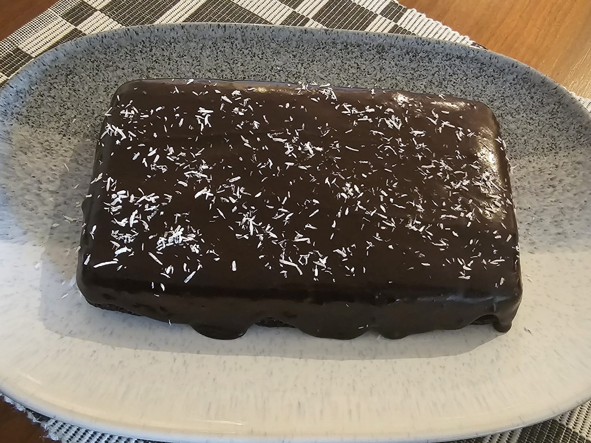 A chocolate frosted cake on a white-grey platter.