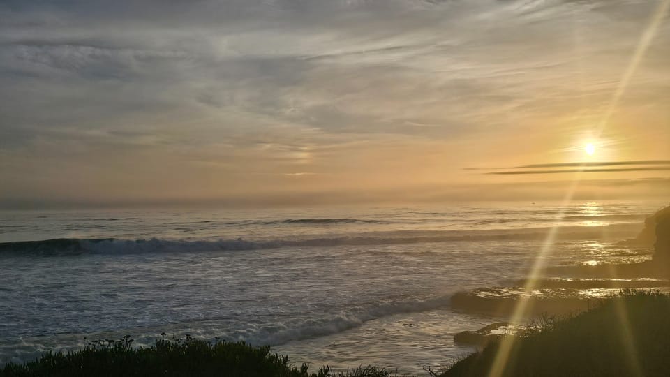 Sun low on horizon of ocean shore and bluff