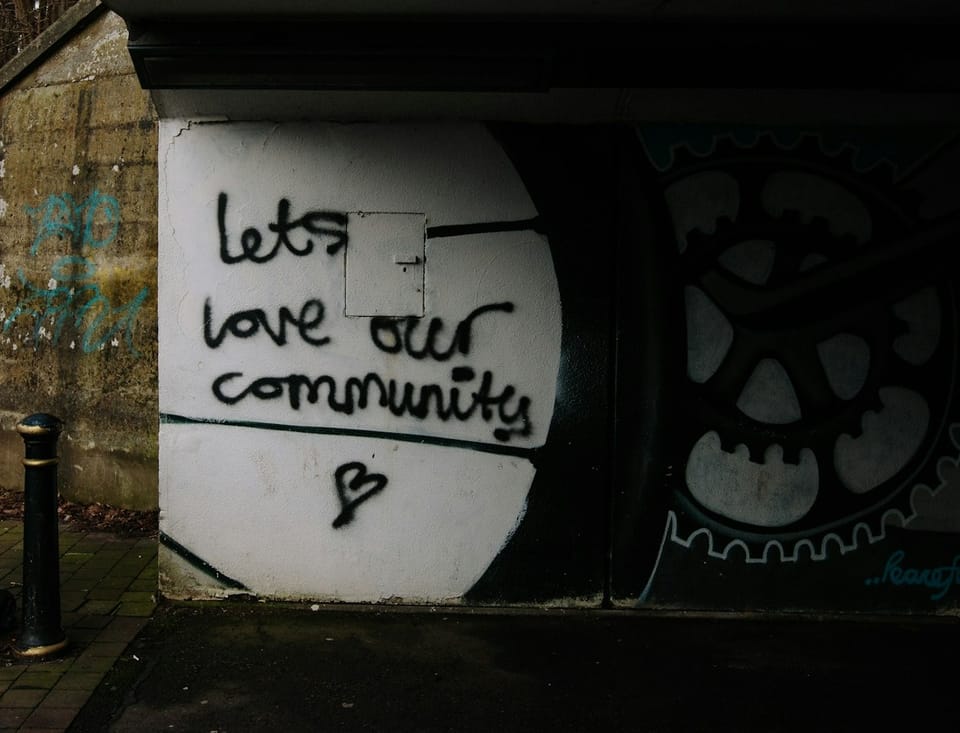 graffiti on tunnel wall of street that reads "lets love our community" with a drawn heart