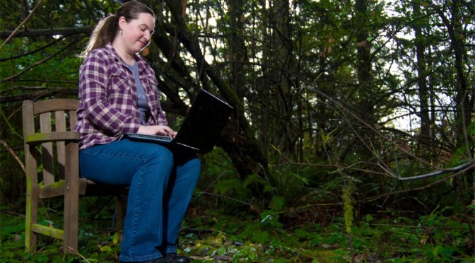 Kate with her laptop in the woods.