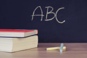 A table with chalk and two books on it. In background is a chalkboard that read "ABC".