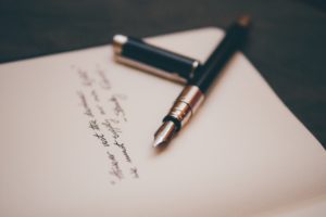 An open notebook with cursive writing in the center and an open fountain pen with lid on top of the page.