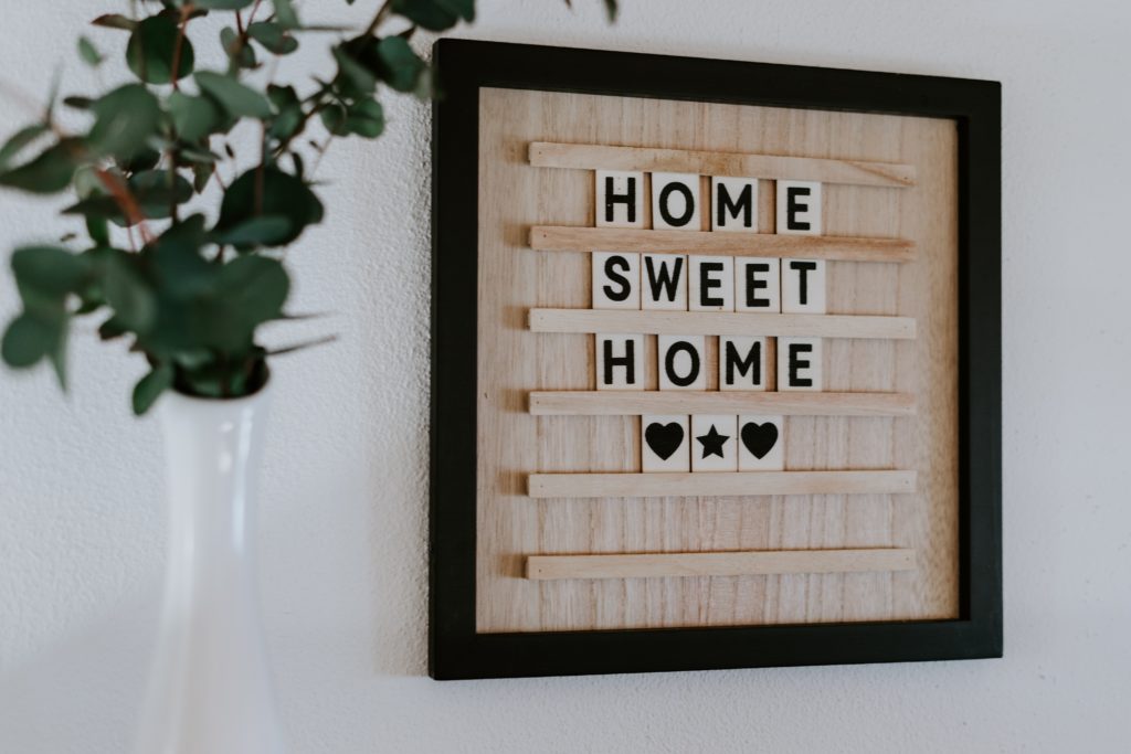 A sign hanging on a wall that reads "Home Sweet Home" and a plant in a vase.