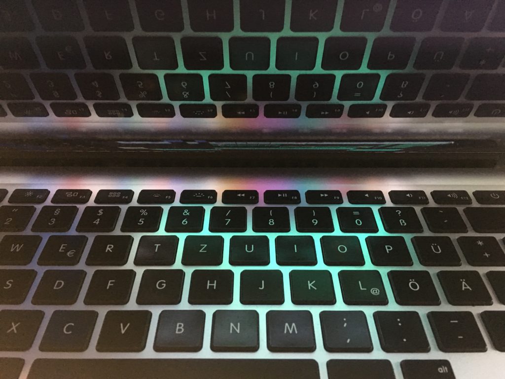 A laptop keyboard with the keys reflected on the screen above. The keys are backlit with a green glow.